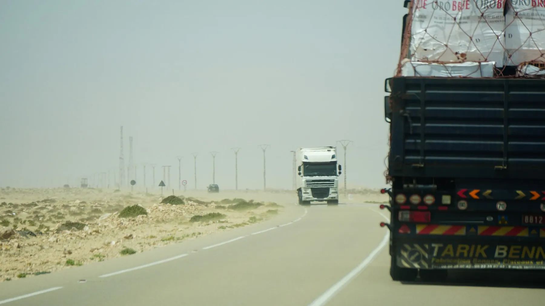 Cargo trucks on a desert highway under a hazy sky