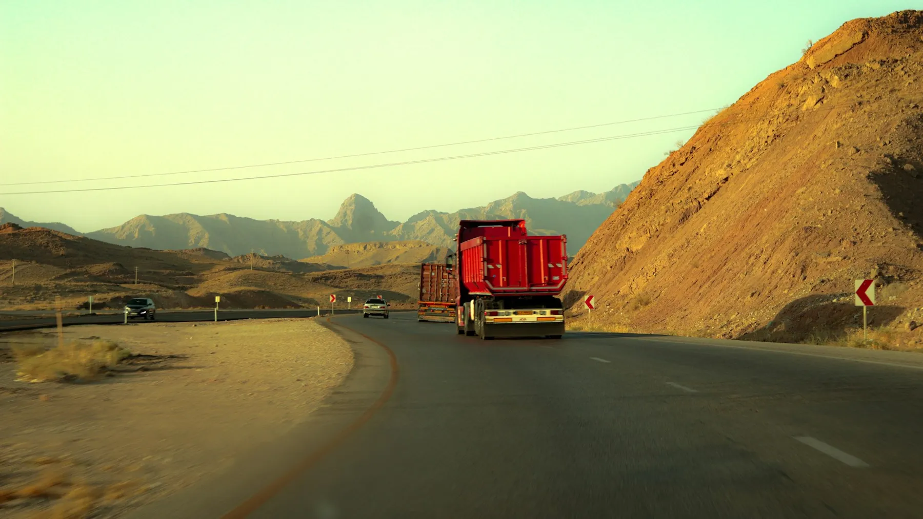 Red truck driving on a desert road through rocky mountains