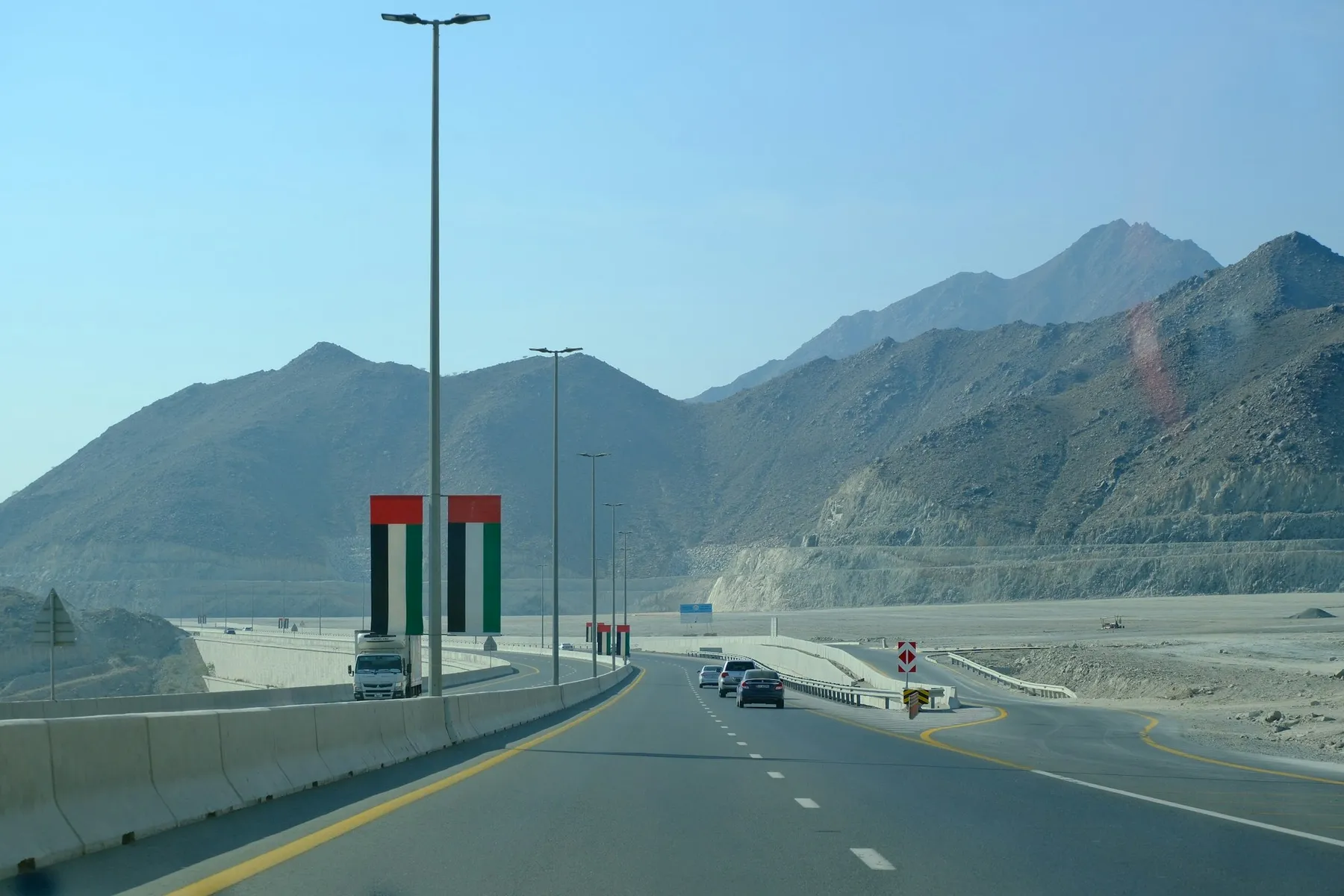 Highway lined with UAE flags leading towards the mountains